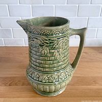Front view showing green glazed pitcher with embossed climbing roses and basketweave pattern
