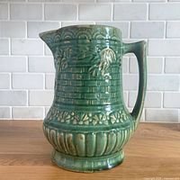 Front view of green glazed stoneware pitcher showing basketweave and floral relief
