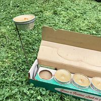 Box opened showing six citronella candles in tins with wire stand assembled