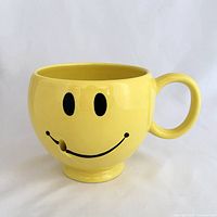 Front view of yellow smiley face mug showing graphic and hole in smile
