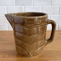 Front view of gloss brown stoneware pitcher showing chevron ribbing and spout
