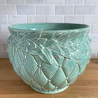 Front view of aqua glazed McCoy jardiniere showing diamond quilted body and leaf motif