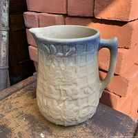 Front view of ceramic pitcher showing embossed pattern and blue fade rim