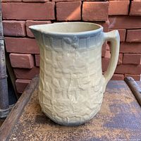 Front view of beige to blue fade embossed climbing rose pitcher on wooden surface