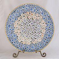 Front view of round mosaic tile dish showing circular blue, purple, rust, and cream tiles with gold rim