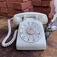 Front angled view of ivory rotary phone showing handset, dial and cords