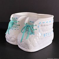 Front angled view of ceramic double baby booties planter showing quilted texture, blue painted stitches, and blue laces