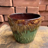 Front view of stoneware planter showing brown to green drip glaze and embossed sun motif