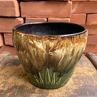 Front view of brown and green drip-glaze stoneware planter showing embossed celestial design