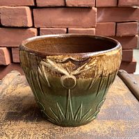 Front view showing brown-over-green drip glaze and embossed sun motif