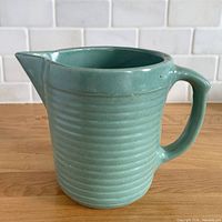 Front view of teal ribbed stoneware pitcher showing spout and body