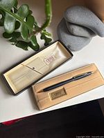 Pen resting in open presentation case beside outer sleeve, showing pen design and case interior