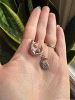 Two silver-plated pendant charms on hand for scale