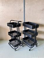 Both black 3-tier metal carts side by side showing overall form and casters