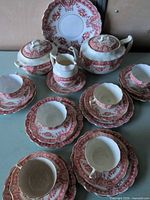 Group view of entire red transferware tea set showing cups, saucers, plates, teapot, sugar bowl, creamer