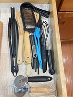 Drawer view of tongs, bamboo spatulas, whisks, grater and pizza cutter