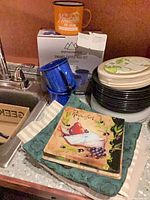 Overall view with enamel mug set box, mugs, leaf plates, black plates, linens and cheese plate