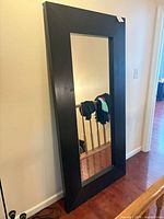 Front view of rectangular espresso-framed floor mirror leaning against wall