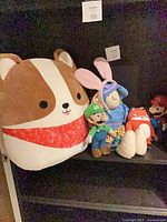 Shelf view showing large dog cushion plush, Luigi plush, blue bunny-eared plush, red car plush and Mario plush