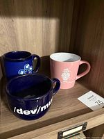 Three ceramic mugs on shelf showing prints and colors