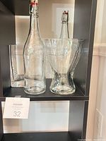 Two swing-top bottles and hourglass vase on shelf