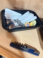 flatware with white handles in black tray alongside corkscrew