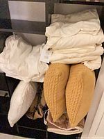 Shelf with folded white bedding, white pillow insert, brown blanket, mustard pillows