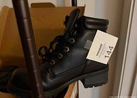 Side view of single black lace-up ankle boot in box with tag