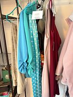 Rack showing turquoise dress, polka dot dress, additional garments, and beige cap