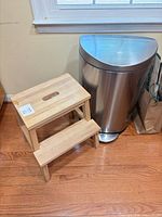 Wood two-step stool beside stainless steel trash can