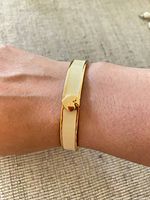 Bangle worn on wrist showing gold-tone edges, ivory enamel band, heart clasp.
