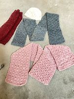 Overview of all five handmade accessories laid flat (pink scarf, cream beanie, red leg warmers pair, grey leg warmers pair)