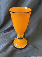 Full view of orange glass vase front side showing flared body, black rim and pedestal base