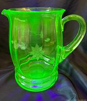 Front view of glowing uranium glass pitcher showing etched flower and faceted base