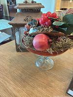 Glass compote with faux fruit and wooden loon beside metal lantern