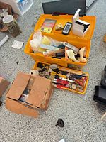 Overview of yellow toolbox, tray and cardboard box with tools and hardware