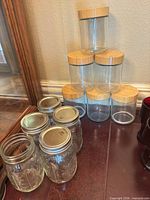 Group view showing four Ball mason jars with metal lids in foreground and six cylindrical storage jars with bamboo lids stacked behind
