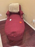 Full view of burgundy striped upholstered chaise lounge with blanket draped over back