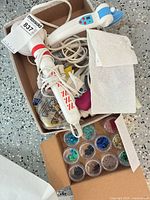 Overview of lot inside box: glue guns, steamer/iron, sequin containers and accessories