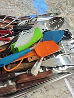 Overview of mixed knives, spatulas, tongs and other utensils spread on countertop