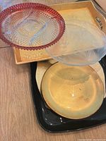 Stacked view of pink pressed glass platter, frosted glass platter, gold charger, black tray, and gold tray