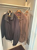Four jackets hanging: black leather, black nylon with grey collar, brown suede leather, beige trench.