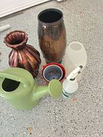 Group view of all six items: watering can, two vases, red planter with insert, spray bottle, clear storage container