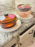 Group view showing amber casserole on white platter, watermelon plates stack, peach bowl, white casserole, clear tumblers