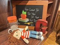 Lot overview showing doll, chalkboard, wooden G, plastic container, mug