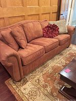Full view of rust terracotta microfiber sofa with three throw pillows and nailhead trim