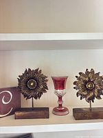 Both sunflower stands and red glass goblet on shelf
