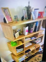 Front view of light oak plywood shelving unit filled with personal items, shows full height and cubby layout