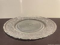 Side view of clear pressed glass plate showing profile, scalloped rim and patterned surface