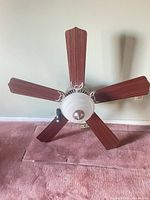 Fan laid on floor showing dark wood blade side, frosted dome light, brushed nickel hub
